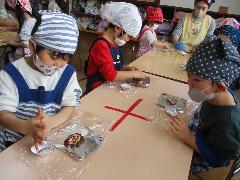 写真：ぱんだ2組の子どもたちが、形作ったクッキーの上に、チョコスプレーなどで飾り付けをしています