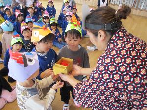 写真：福の神に変装した職員が、折り紙で作った梅の花を代表の3人の子どもたちに手渡しています。