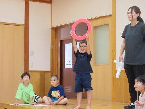 写真：夏野菜クイズを出題する5歳児。丸形の赤い枠を頭の上に掲げています。