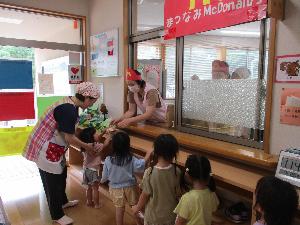 写真：給食室の前に一列に並び、給食室の先生からハンバーガーを受け取る2・3歳児