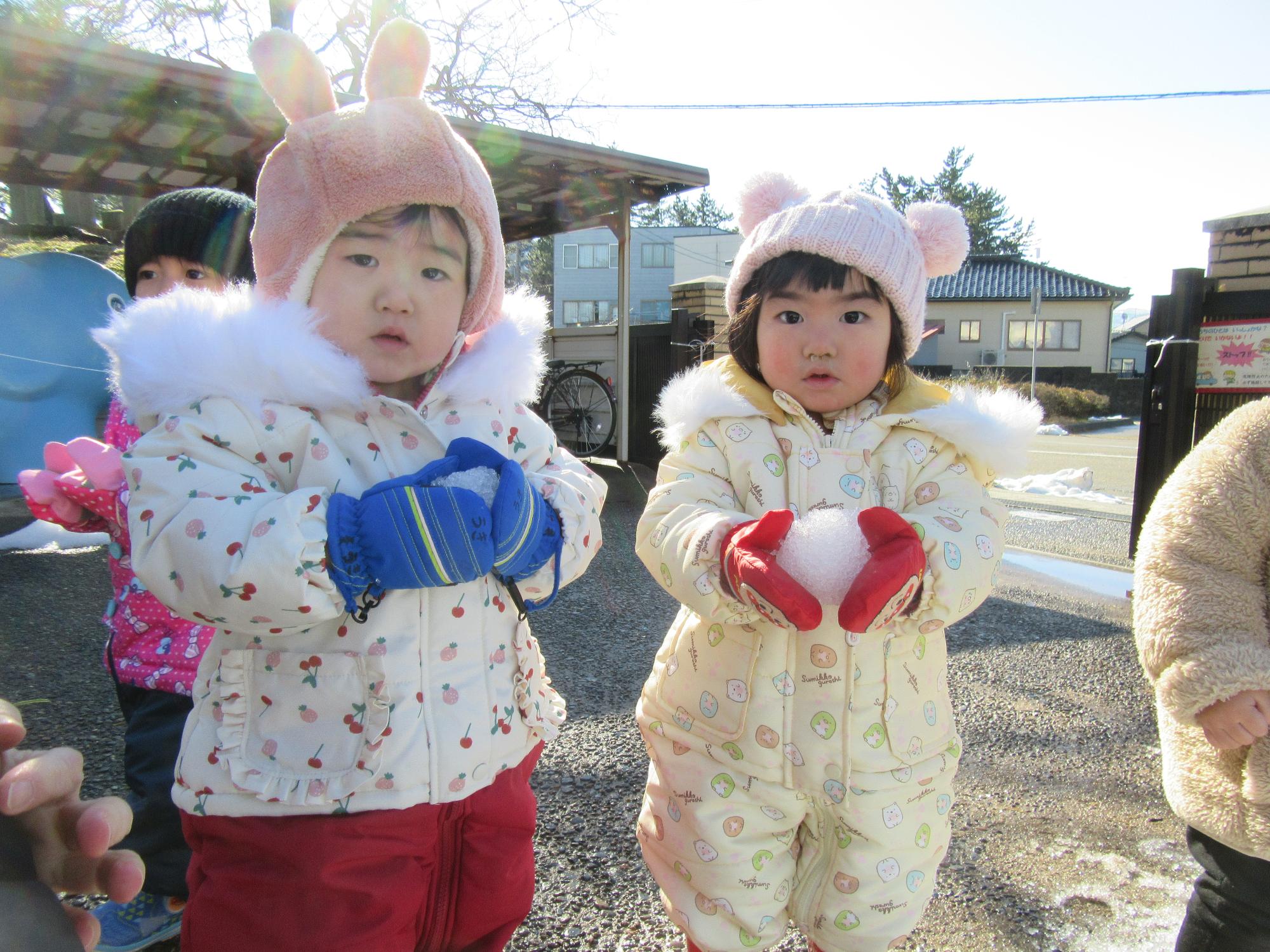 写真：1歳児の子ども達が園庭で雪を手に持っています