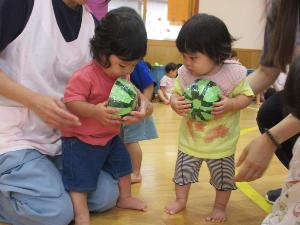 写真：すいかわりゲームのスイカを持つ0歳児。一人はできもののスイカをかじろうとし、もう一人は胸の前に大事そうに抱えています。