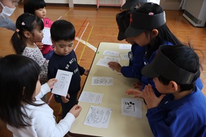 写真：郵便ごっこで年賀状を買いに来たうさぎ組2歳児。机に並んだ年賀状の中からお気に入りの絵柄を選んでいます。