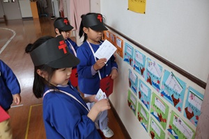 写真：郵便マークのついた帽子をかぶった年長児が、廊下の状差しに年賀状を配達しています