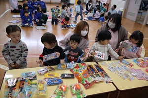 写真：当たりハガキを手にずらりと並んだ景品を選ぶりす組（0・1歳児）の子どもたち