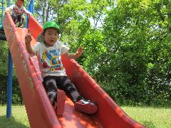 写真：赤い滑り台をいきおいよく滑りおりる4歳児。