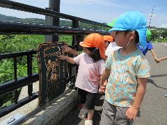 写真：鯖石橋の欄干に設置された鯖カッパのモニュメントを触る散歩中の4・5歳児。