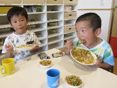 自分たちで作ったカレーを大きな口を開けて美味しそうに食べるきりん組男児二人の写真。