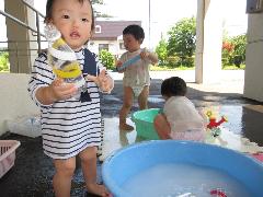 写真：たらいに水を溜めて、空き容器の中に水を入れたり出したりして遊ぶ1歳児