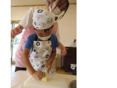 調理保育のためエプロンを付けた5歳児男児が保育士に付き添われ、ジャガイモを包丁で切っている様子の写真。