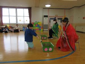 写真：園児がひなあられに見立てたボールをお玉にのせて、おひなさまの前に置いてあるかごに運び入れるゲームをしているところ