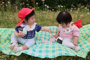 写真：草の上にレジャーシートを広げ、りす組の子ども2人がおままごとのおにぎりを持っています