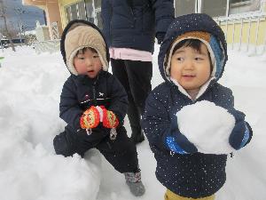 写真：自分の顔ほどの大きさの雪玉と、手のひらサイズの雪玉を持った2人の子どもたち。これから雪だるまを作ろうをしているところです。