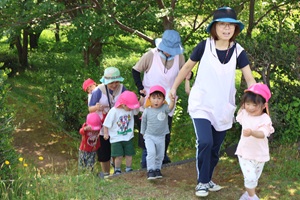 写真：保育者や子どもたち同士で手をつないで夕日の森公園の森の中を散歩しているところ