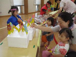 写真：チョコバナナのお店にお買い物に来たりす組の女の子二人と、法被を着たチョコバナナ屋さんのらいおん組の女の子が向かい合っているところ