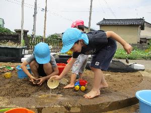 写真：年長児が砂場の穴に水を入れている様子