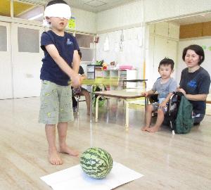 写真：スイカ割りをしているところ。目隠しをした年長児が、棒を持ってスイカの前で構えています。