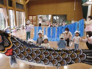 2歳児が滝に見立てた水色のスズランテープをくぐり、こいのぼりにタッチするレースをしている写真