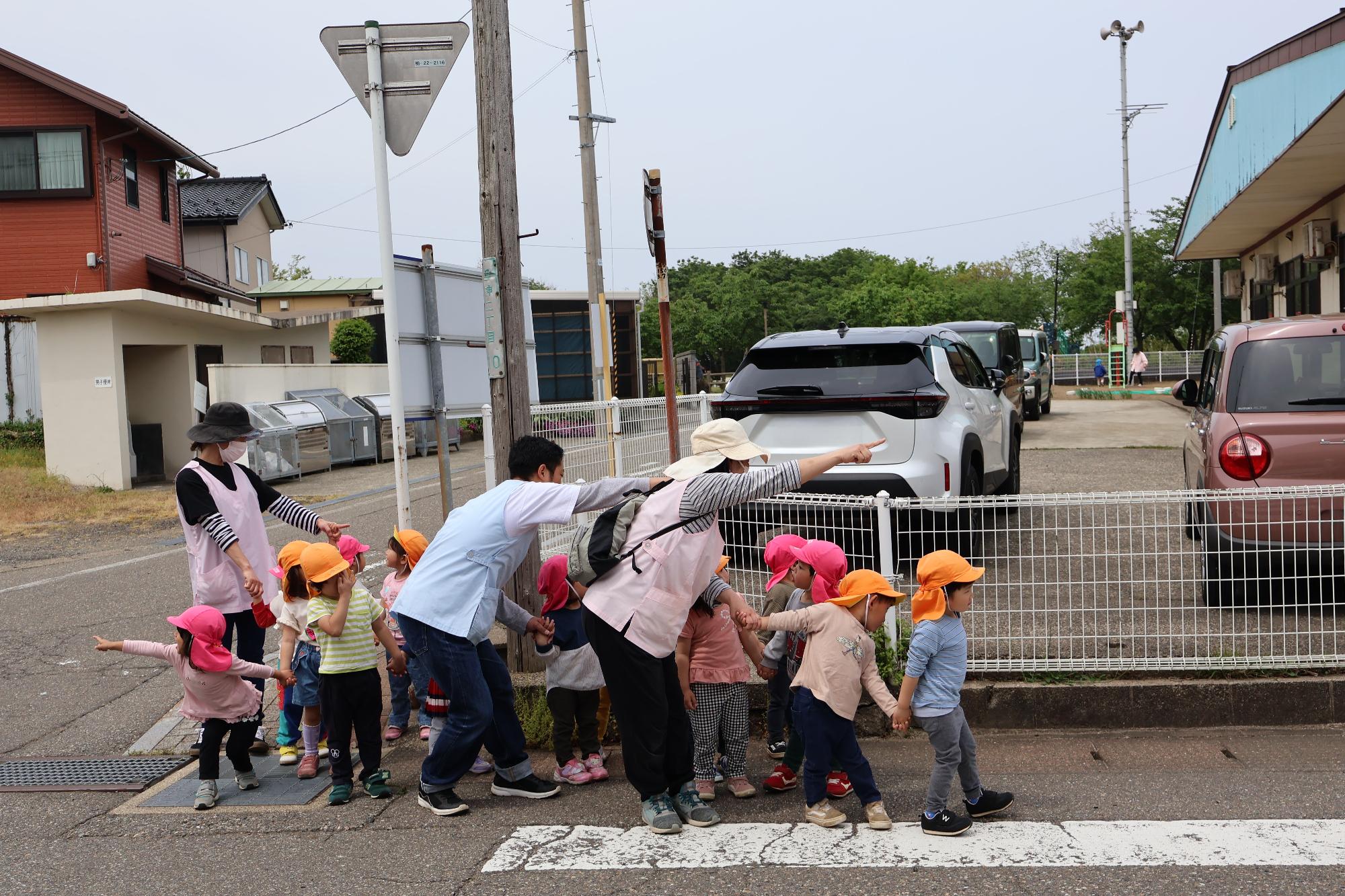 写真：保育士に付き添われながら、横断歩道を渡る前の左右確認をしている子どもたち