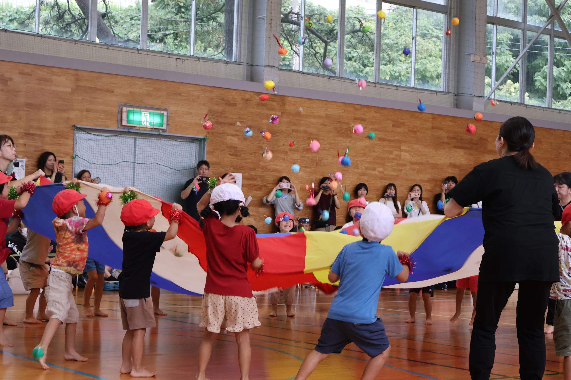 写真：バルーンの端を引っ張ったり緩めたりして、バルーンの上にあるたくさんのボールを弾いている子どもたち