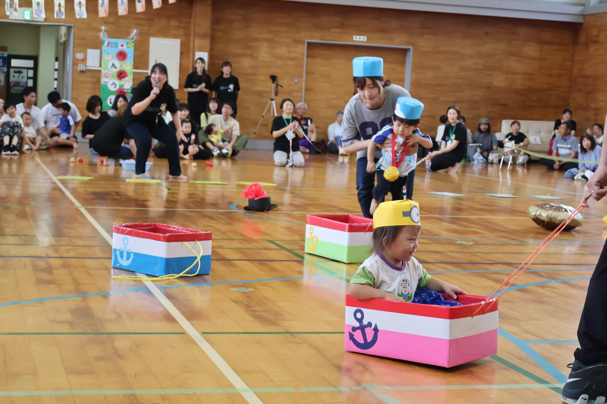 写真：親子で変装し、段ボールで作った船に乗った子どもを保護者が引っ張って競争しています。