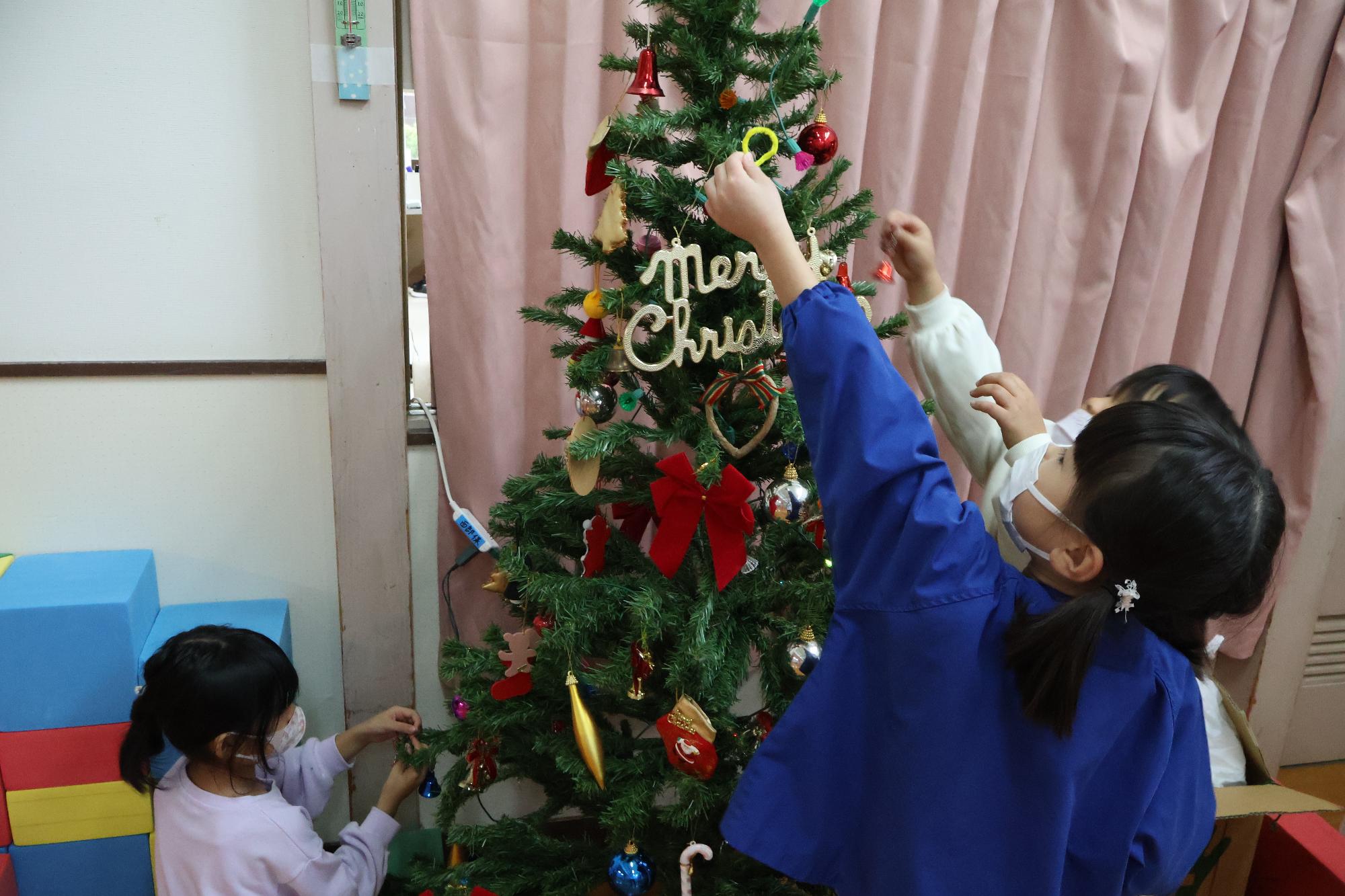 写真：大きく背伸びをして、クリスマスツリーに飾りをつける女の子