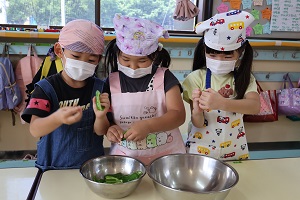 写真：年長児3人ががピーマンの種を取っているところ。