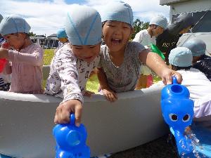 写真：ぱんだ組の子どもたちがジョウロを使ってプール遊びを楽しんでいます。