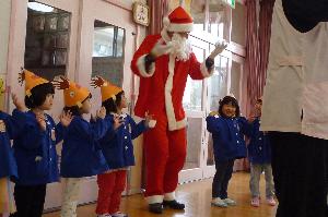 写真：トナカイの帽子をかぶったぞう組の子どもたちとサンタさんが一緒にフォークダンスを踊っている