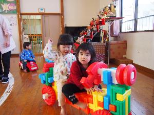 写真：遊戯室で遊ぶひよこ組の子ども達。ブロックで組み立てた車に乗っています
