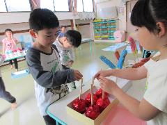 縁日ごっこでりんご飴をお友達から買っている園児の写真
