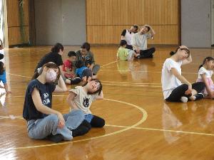 写真：親子で横並びに座り、片手を頭に乗せ首を横に傾けてストレッチをしています