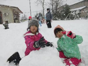 写真：雪の上に膝をつき、2人の年長児が雪山を作っています