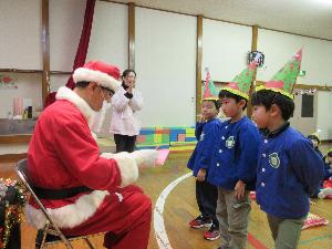 写真：椅子に腰かけたサンタクロースに、3人の年長児がお礼の手紙を渡しているところ