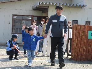 写真：保育園前の道路で横断の練習をする園児と保護者。園児は右手を大きく上げ、保護者としっかり手をつないでいます