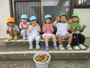 写真：バケツ一杯に入った収穫したばかりのジャガイモを前に、1列に並んで笑顔を見せるぞう組の子どもたち