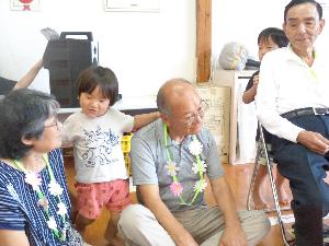 写真：祖父母の間に立ち、2歳児男児が片手ずつで祖父母の肩を叩いているところ