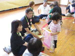 写真：2歳児女児が祖父母と向かい合い、プレゼントを渡そうとしているところ。
