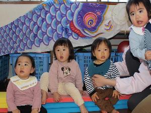 写真：お遊戯室の壁に飾ったこいのぼりの前に並んぶ4人の子どもたち