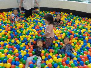 写真：5人の園児がボールプールの中で遊んでいます。カラーボールの上に寝転んで笑顔を浮かべている子どももいます。