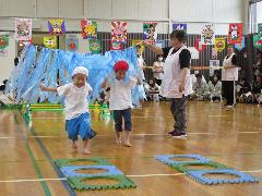 コミセンの体育館を2人の子どもが障害物競走で滝に見立てた平テープをかき分けて走り抜け、次の障害物に向かって走っている写真