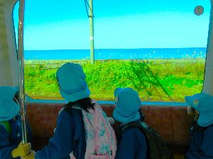 写真：車窓から見えた日本海を眺める子どもたちの後ろ姿。水色のお揃いの帽子を被り、リュックサックを担いでいます。穏やかな日本海と、真っ青な空が広がっています