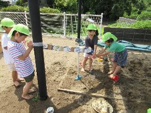 写真：園庭の砂場に牛乳パックをつなげて水道管を作り、水を流して遊んでいる4歳児たち