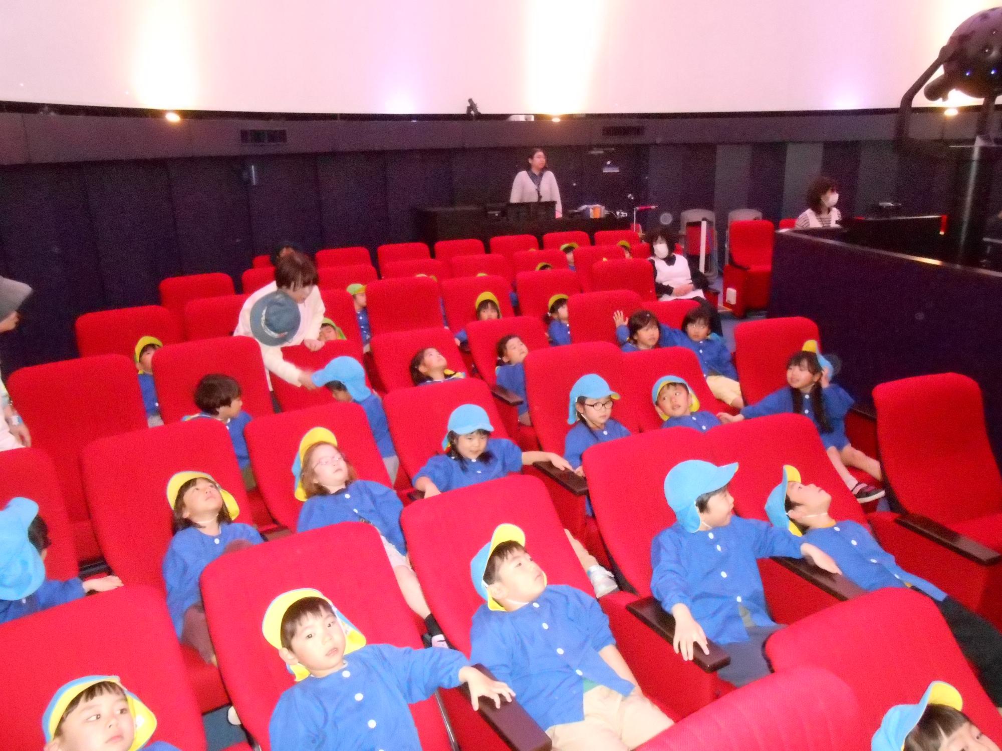 写真：らいおん組の子どもたちが、プラネタリウムの椅子をリクライニングさせ、天井に映る映像を眺めているところ