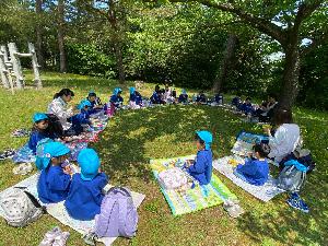 写真：木陰にレジャーシートを広げて、お弁当を食べているぞう組の子どもたち
