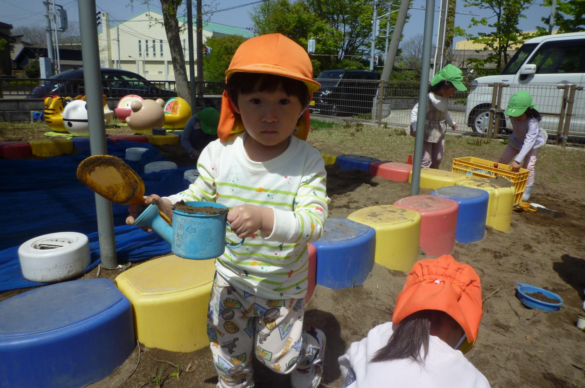 写真：スコップとミニじょうろを持ち砂遊びを楽しむぞう組の子どもたち