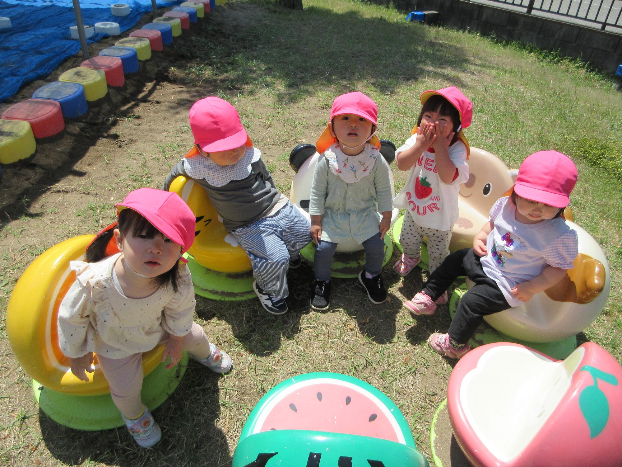 写真：うさぎ組の子どもたちが園庭のいすに座っています。いすには果物や動物の顔がプリントされています。