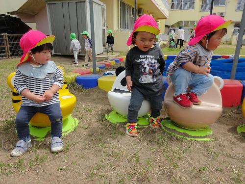 写真：園庭に置かれた動物の形のベンチに座る3人の1歳児