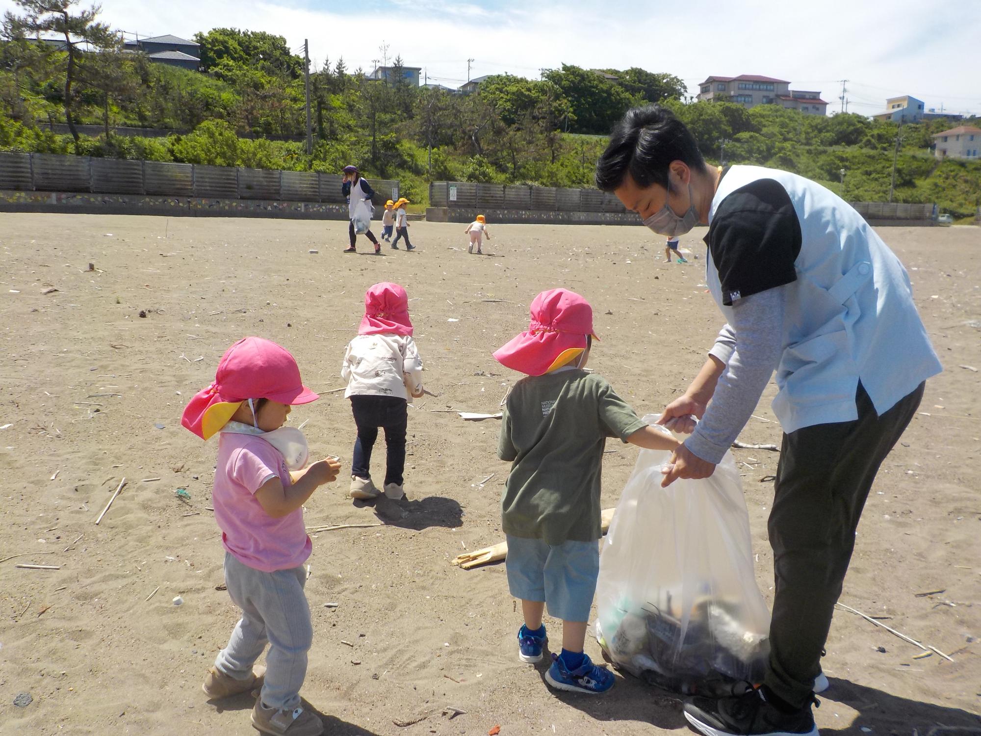 写真：子どもたちが拾ったゴミを保育士の持つビニール袋に集めているところ