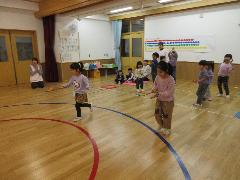 写真：子ども達が羽子板の上のままごとのみかんを乗せて落とさないように運ぶリレー形式のゲームをしているところ